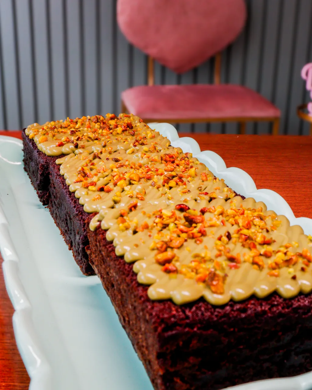 Brownies em fila numa travessa, com cobertura cremosa e confeitos, e uma poltrona de coração ao fundo.