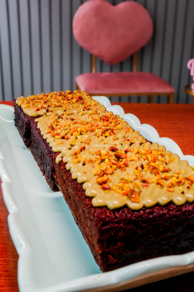 Brownies em fila numa travessa, com cobertura cremosa e confeitos, e uma poltrona de coração ao fundo.