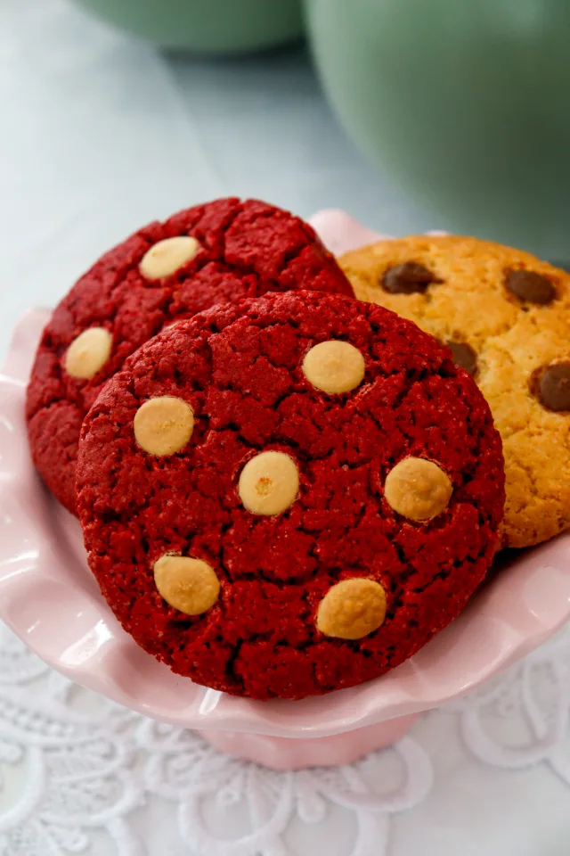 Cookies vermelhos com gotas brancas e cookies com gotas de chocolate num prato rosa.