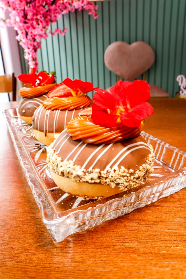 Donuts com cobertura de chocolate, creme e flores vermelhas numa travessa de vidro.