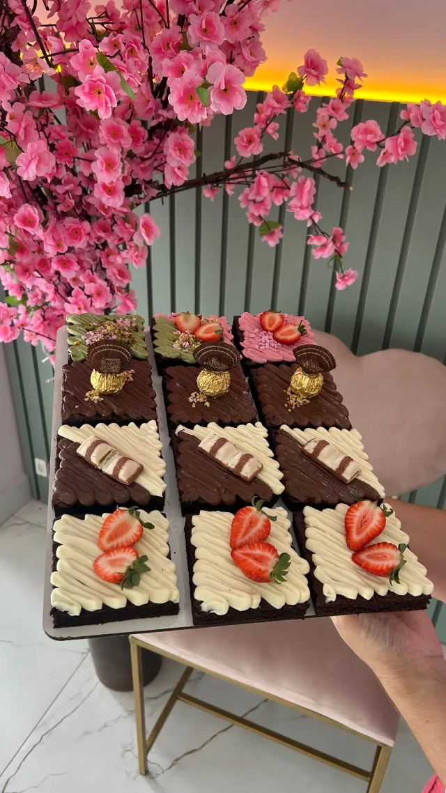 Bandeja com nove quadrados de bolo de chocolate em três coberturas: bombom dourado, barrinha de chocolate e creme com morangos.