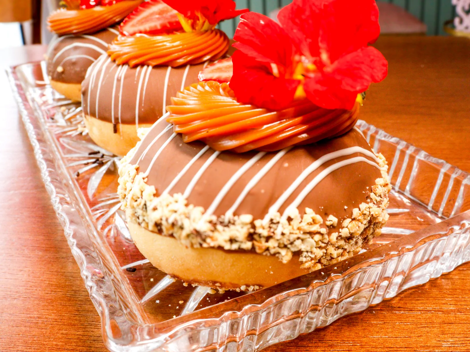 Donuts com cobertura de chocolate, creme e flores vermelhas numa travessa de vidro.