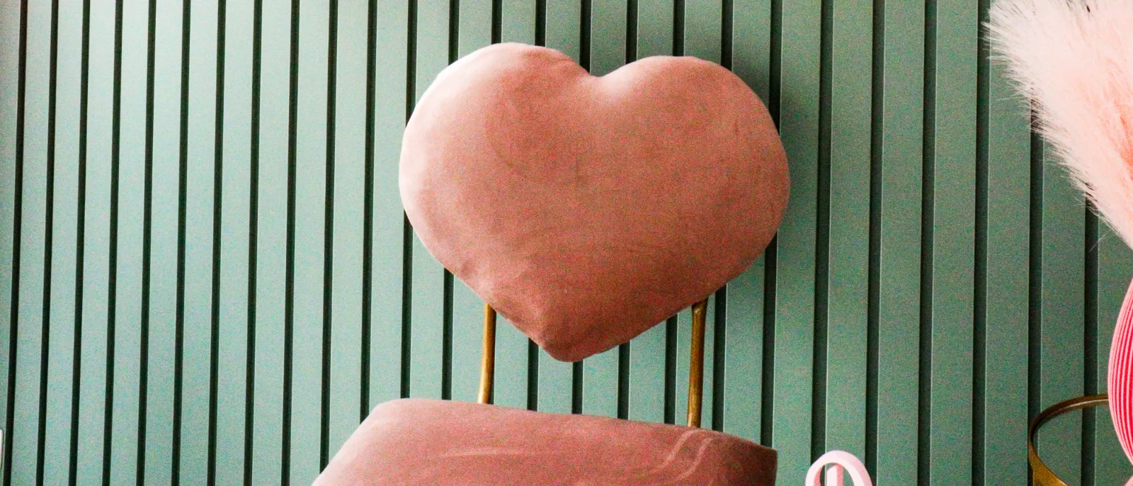 A poltrona de coração em veludo rosa diante do painel ripado verde do salão.