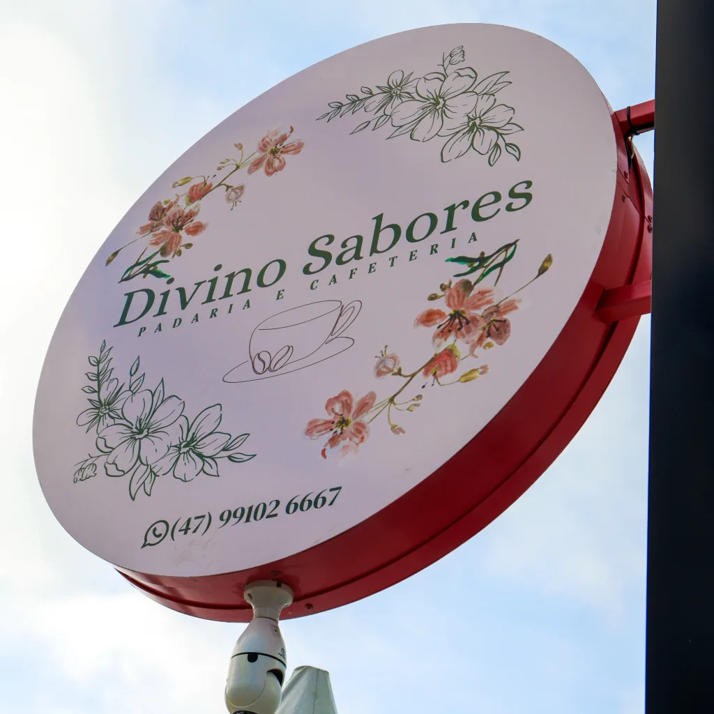 A placa redonda da Divino Sabores na fachada, com a logo, a coroa de flores e o WhatsApp da casa.