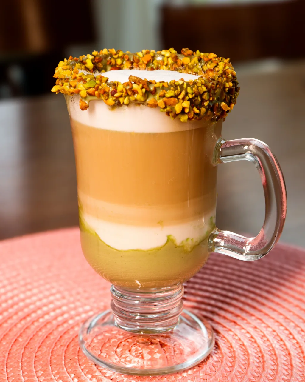 Café em camadas na caneca de vidro, com a borda coberta de pistache.